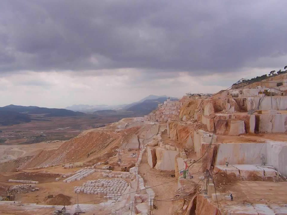 Rocky quarry under a cloudy sky with distant mountains.