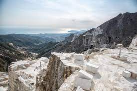 Quarry with white marble blocks against a mountainous backdrop.